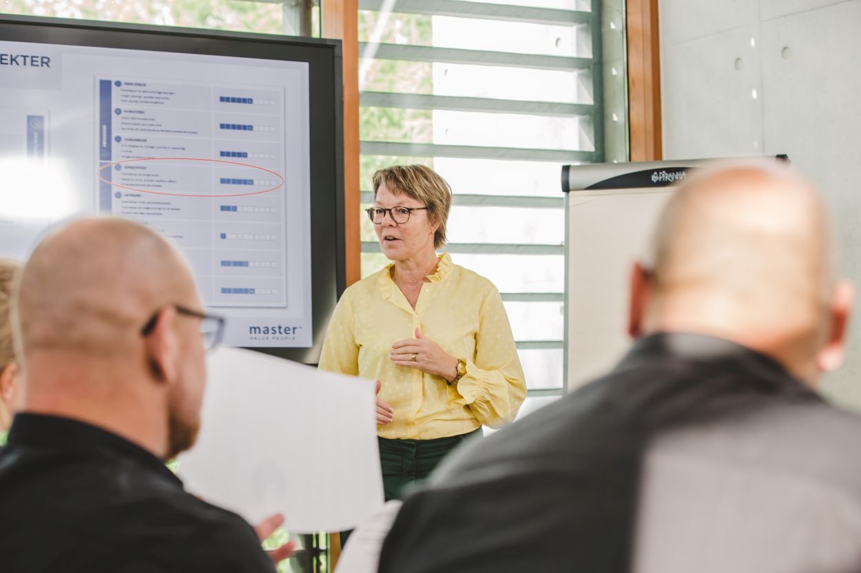 enior businesswoman in a yellow blouse presenting on a projector to team members in the room.